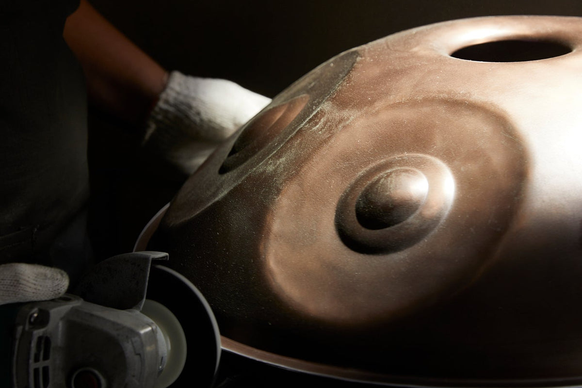 Eine Hand in Arbeitshandschuh hält eine Handpan-Schale mit dem Ding in der Werkstatt
