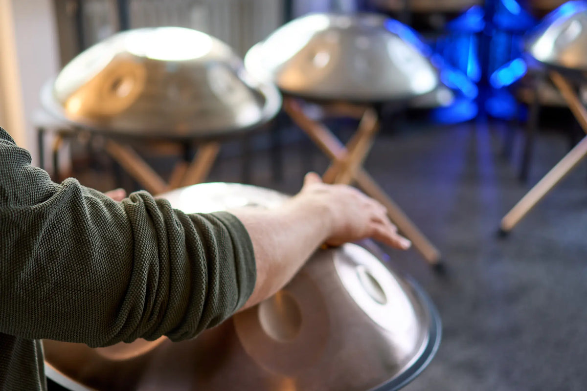 Eine Hand liegt auf einer Handpan, dahinter weitere Handpans auf Ständern