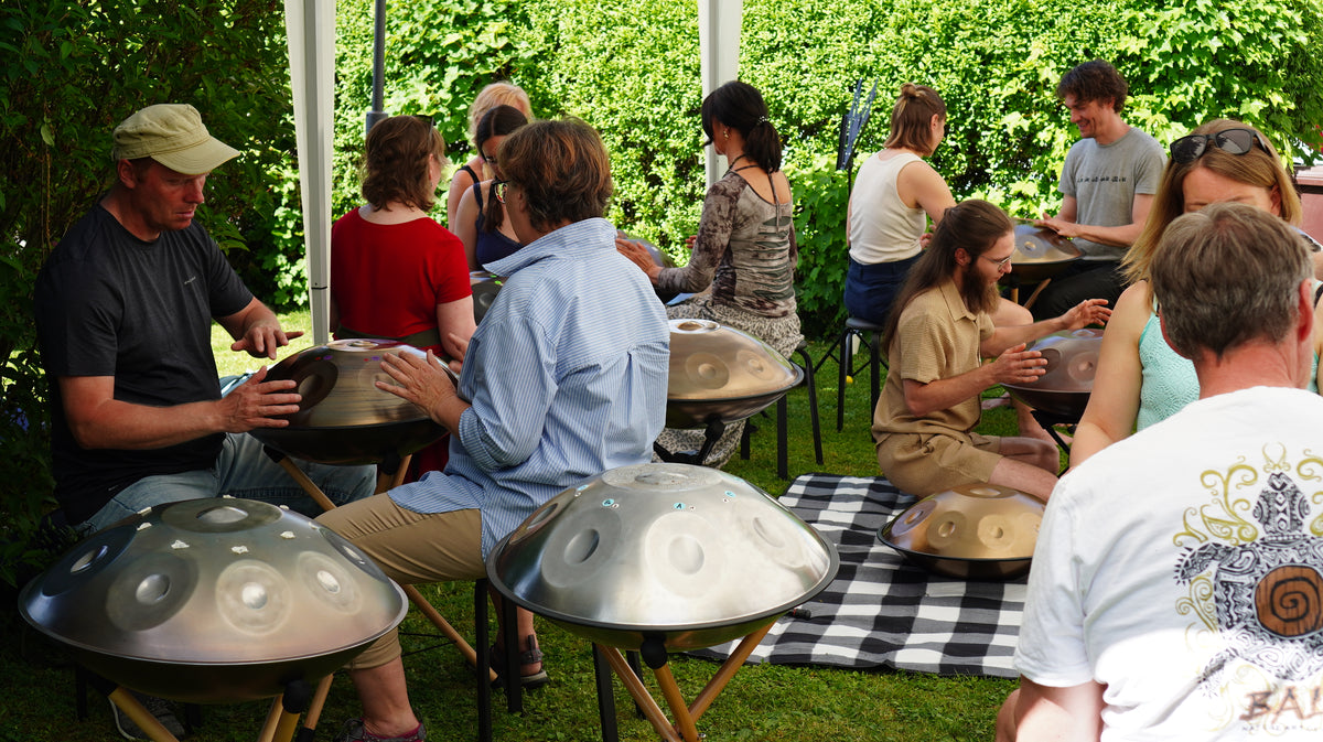 Eine Gruppe spielt gemeinsam Handpan im Garten, die Instrumente stehen auf Ständern