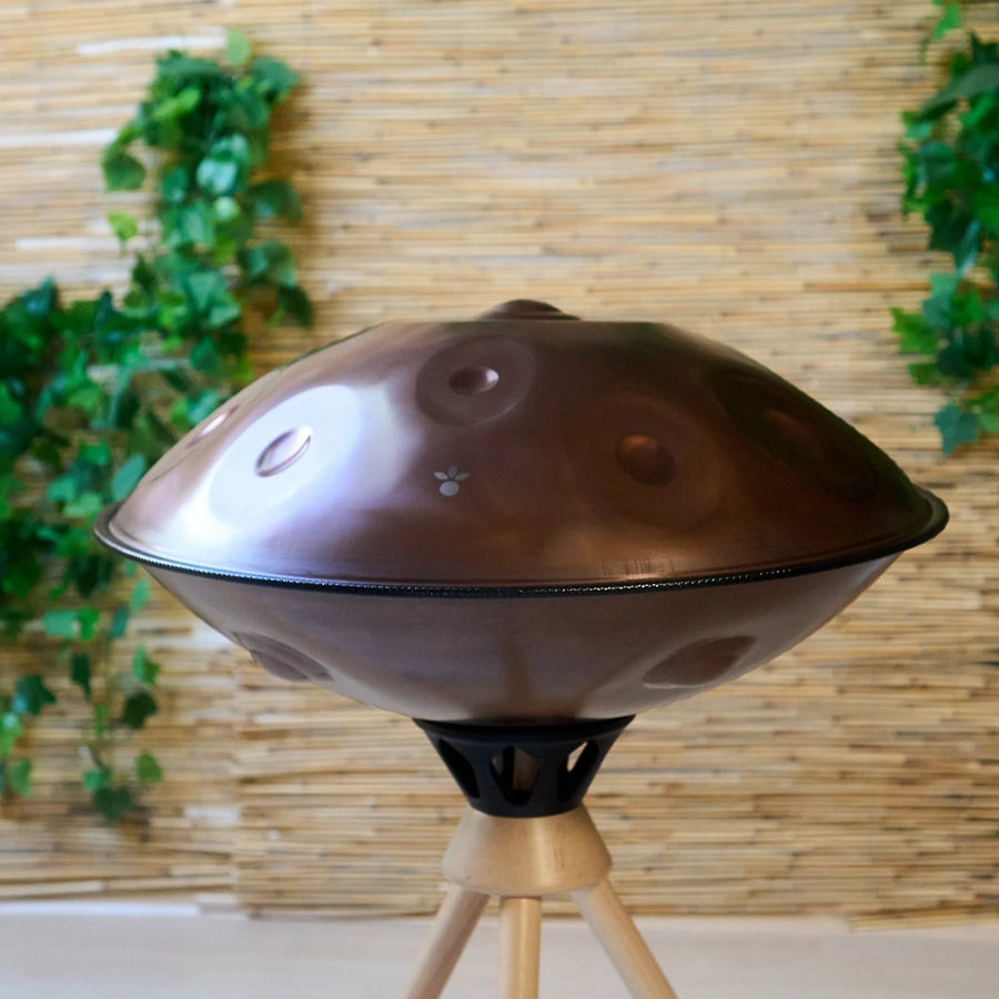 Handpan D Kurd 10 auf Holzständer, Frontansicht vor Bambuswand – kupferbraunes Finish, handpanladen