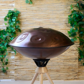 Handpan D Kurd 12 auf Holzständer, Seitenprofil vor Bambuswand – kupferbraunes Finish, handpanladen